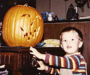 Toddler boy looking a bit wary of a carved pumpkin.