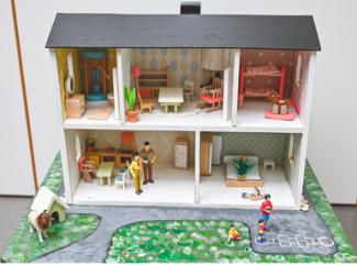 A dollhouse, open in front with two stories, furniture in rooms and people in front